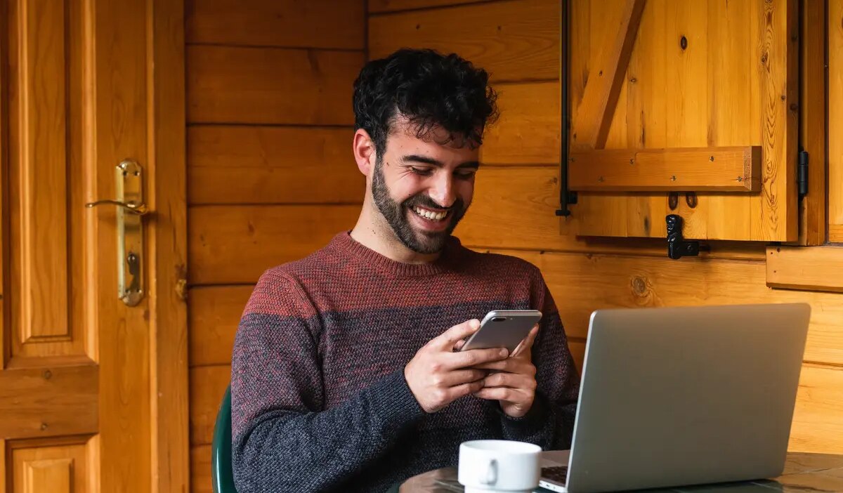 Cheerful man browsing on smartphone and working on terrace