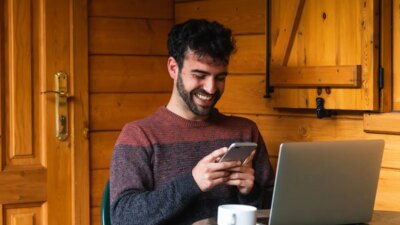 Cheerful man browsing on smartphone and working on terrace