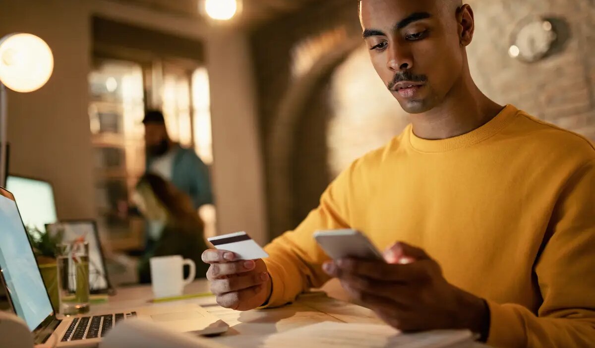Young black businessman using credit card and smart phone while shopping online in the office