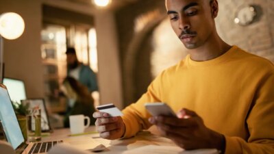 Young black businessman using credit card and smart phone while shopping online in the office