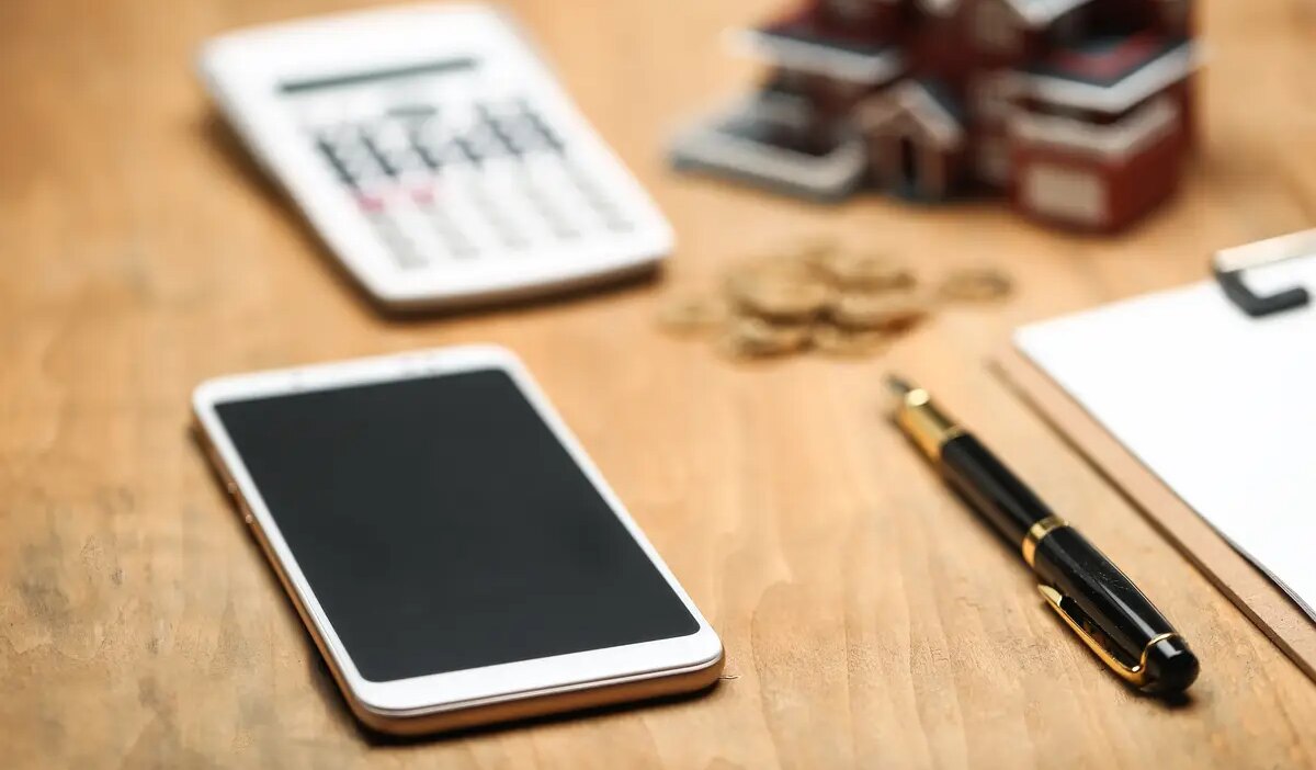 house model ,smartphone ,calculator and golden coins on wooden table
