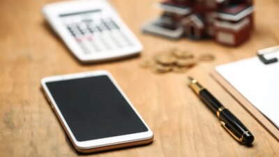 house model ,smartphone ,calculator and golden coins on wooden table