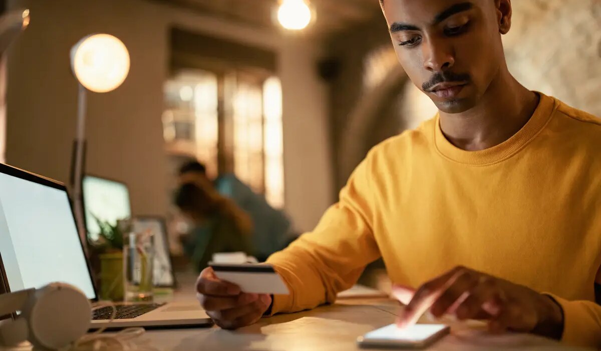 African American businessman using credit cart and mobile phone while checking his online bank account during late night work in the office