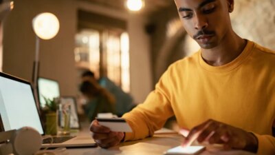 African American businessman using credit cart and mobile phone while checking his online bank account during late night work in the office